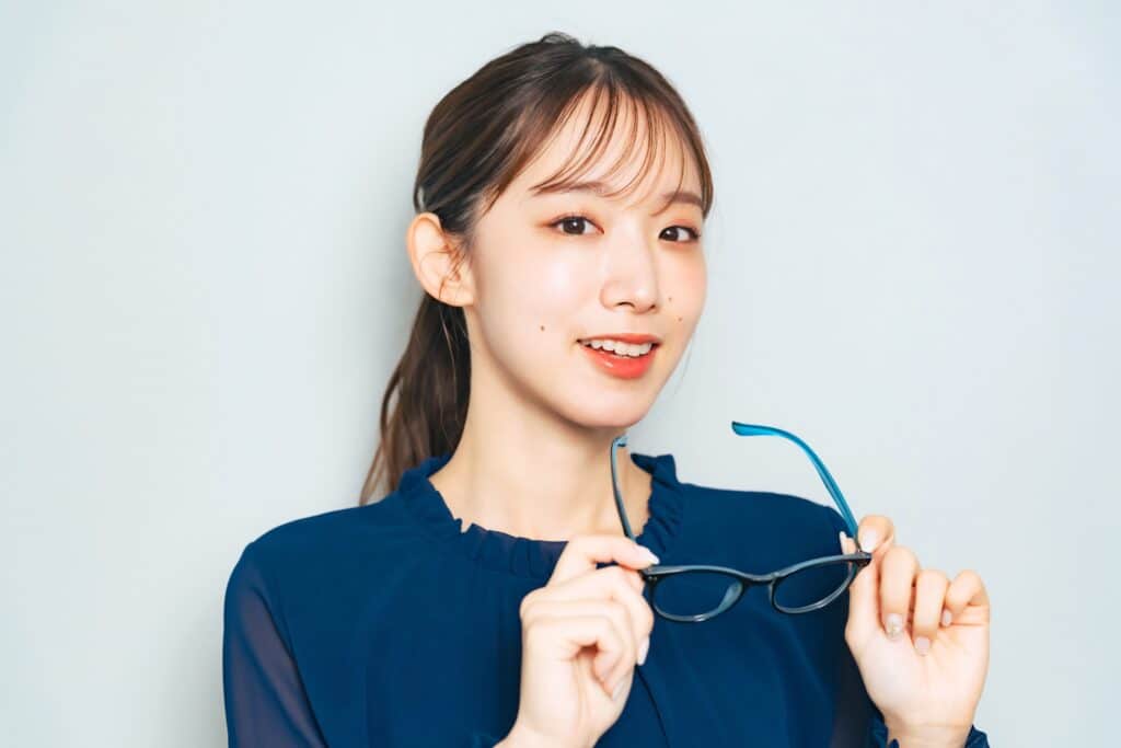 A young woman smiles while holding her glasses, enjoying clearer vision after orthokeratology treatment