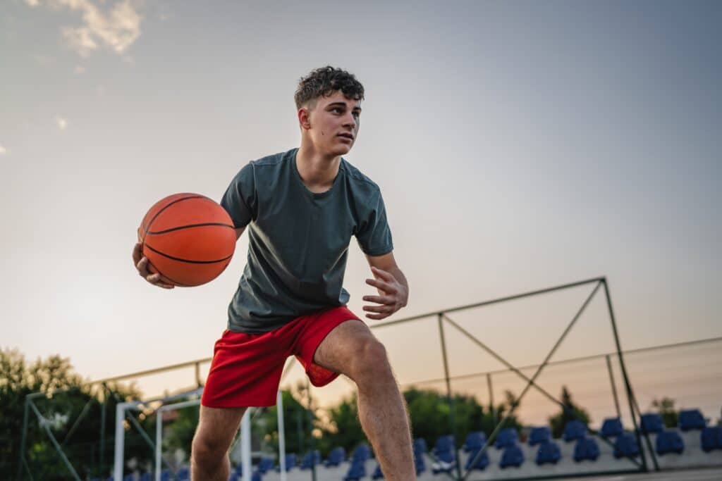 Teenage boy standing on basketball court in the evening holding ball, ready to play game with copy space.