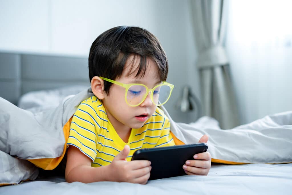 Child wearing glasses and using a smartphone, illustrating myopia progression in children.